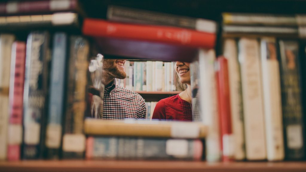 Two people talking behind stacked books in a library