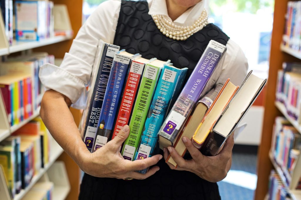 A woman holding a large stack of library books.