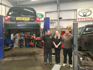 Inside Barle JM Motors. There is a car raised up ready to be worked on. Three staff are standing in the middle.