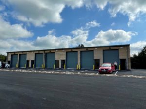 An outside view of the units with sectional doors. There are marked spaces for parking and loading outside.