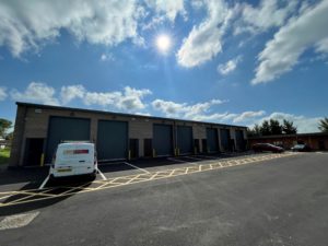 An outside view of the units with sectional doors. There are marked spaces for parking and loading outside.