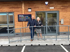 An outside view of the entrance to the office space. The building is clad in horizontal wood panels and there is an accessible ramp leading to the front door. A man and woman are standing outside.