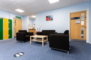 Office meeting area with three arm chairs in a U shape around a low wooden table. There are lockers on one wall.