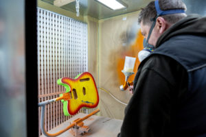 Man wearing a protective mask spray painting body of guitar