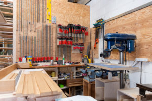 An inside view of the workshop. There's a range of tools on the walls and a pillar drill.