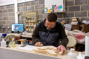 Man creating wooden guitar body in a workshop space