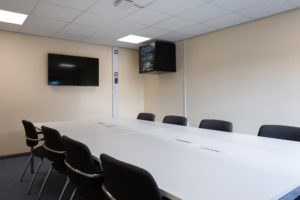 Wells meeting space. There is a large desk with 8 chairs around it. There is a screen mounted on one wall.