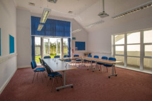 Inside view of a Williton enterprise centre large meeting room. The desks are arrange in a U shape. There are large floor to ceiling windows on two walls.