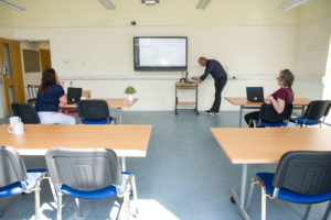 Inside view of a Williton enterprise centre meeting room. There are four 2-person desks visible. There is an interactive white board screen on one wall.