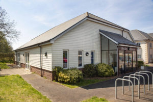 Outside view of Williton enterprise centre. There are bars for bicycle storage and a large glass porch. A tarmac footpath surrounds the building.