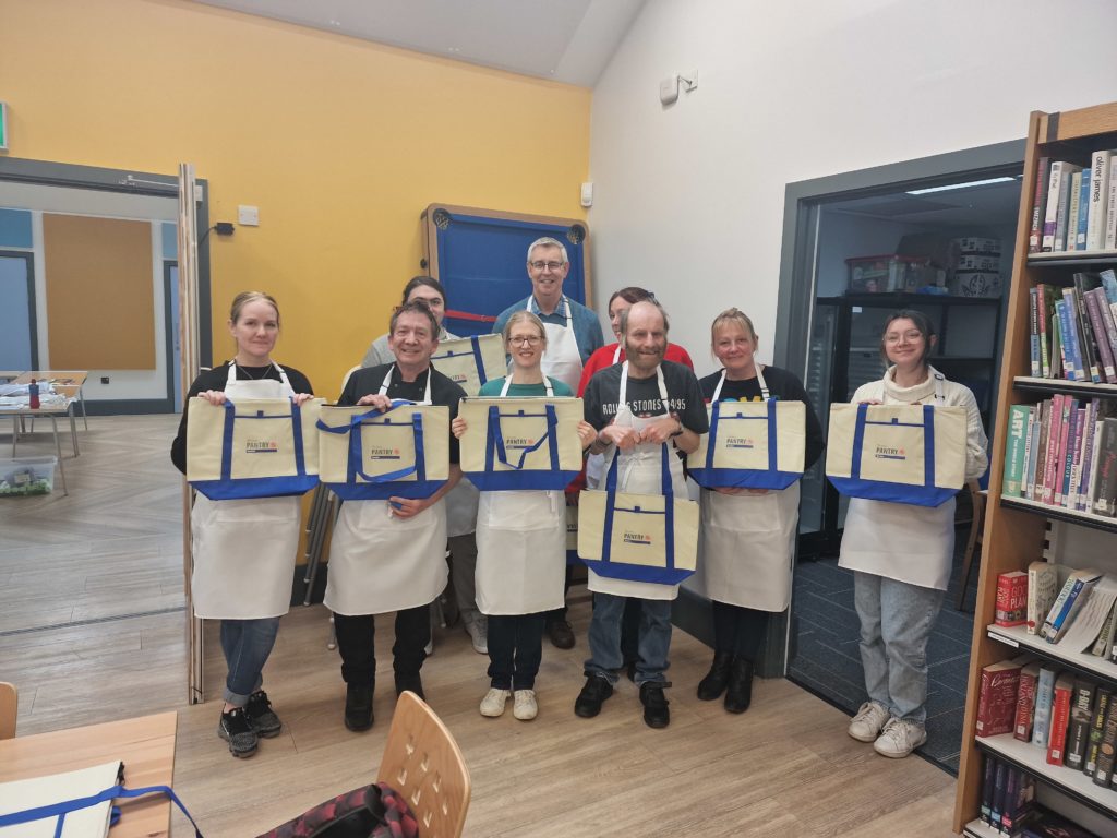 Group of people standing together each holding a hessian bag with the local pantry logo on them.