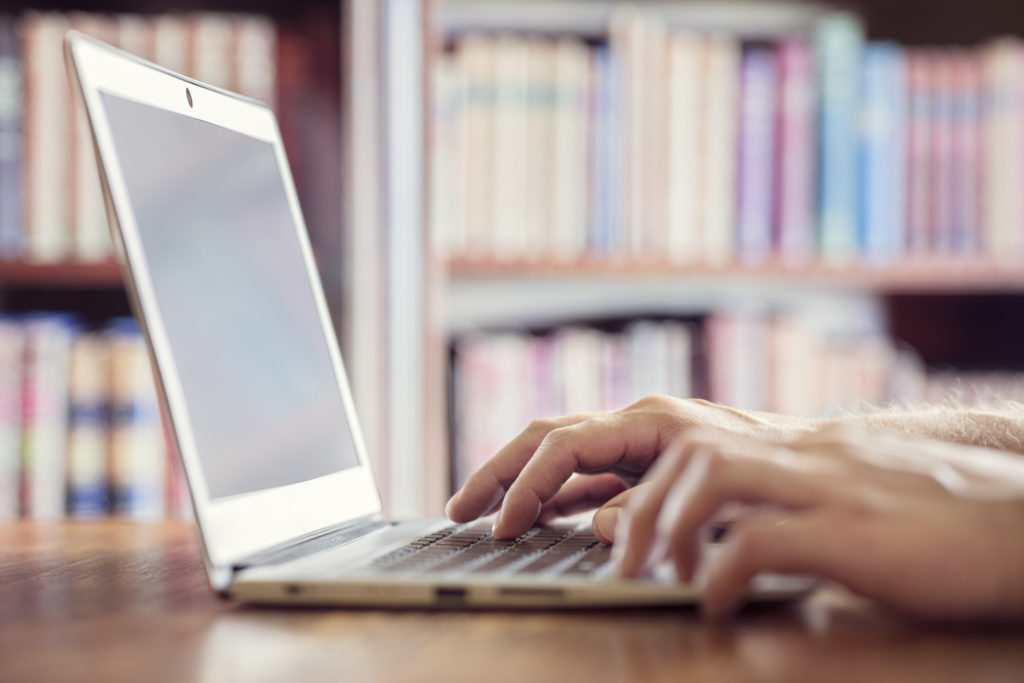 Hands typing on laptop computer in library