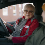 Val is sitting in the drivers seat, talking to a passenger