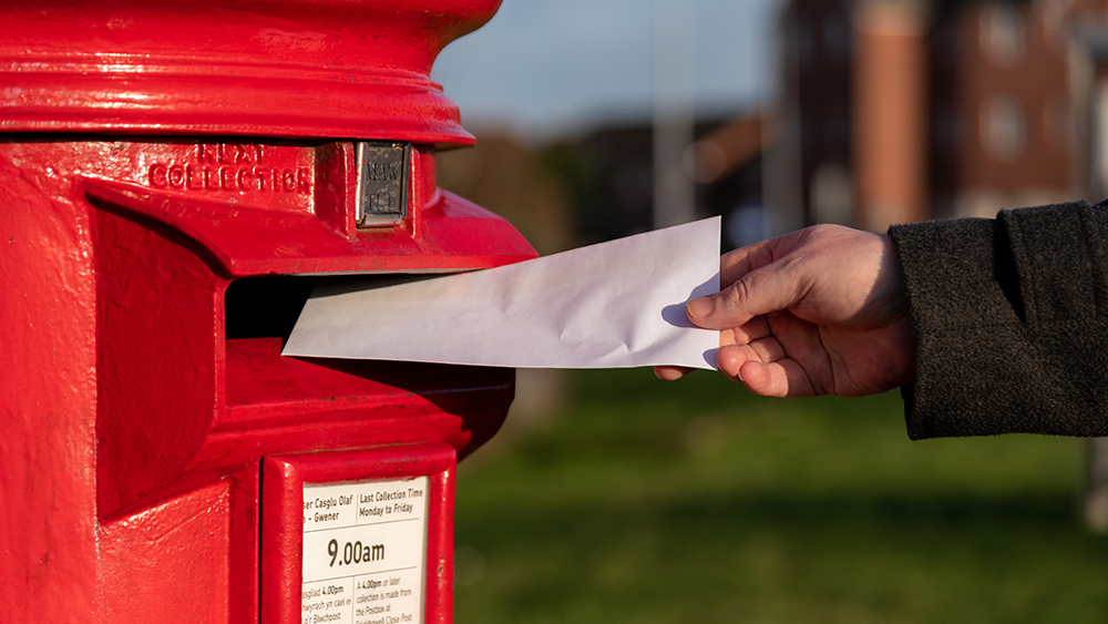 A classic Royal Mail postbox with someone posting a document