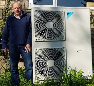 A man stood next to a air source heat pump fitted at his home
