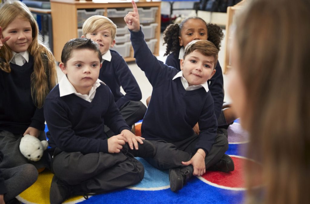 Special needs children in uniform sat cross-legged being taught at school.