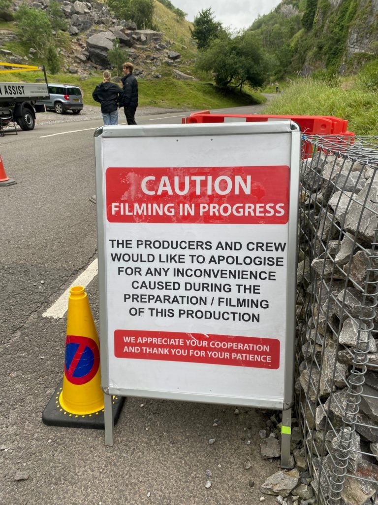 An A frame sign situated at Cheddar Gorge stating caution. filming in progress.