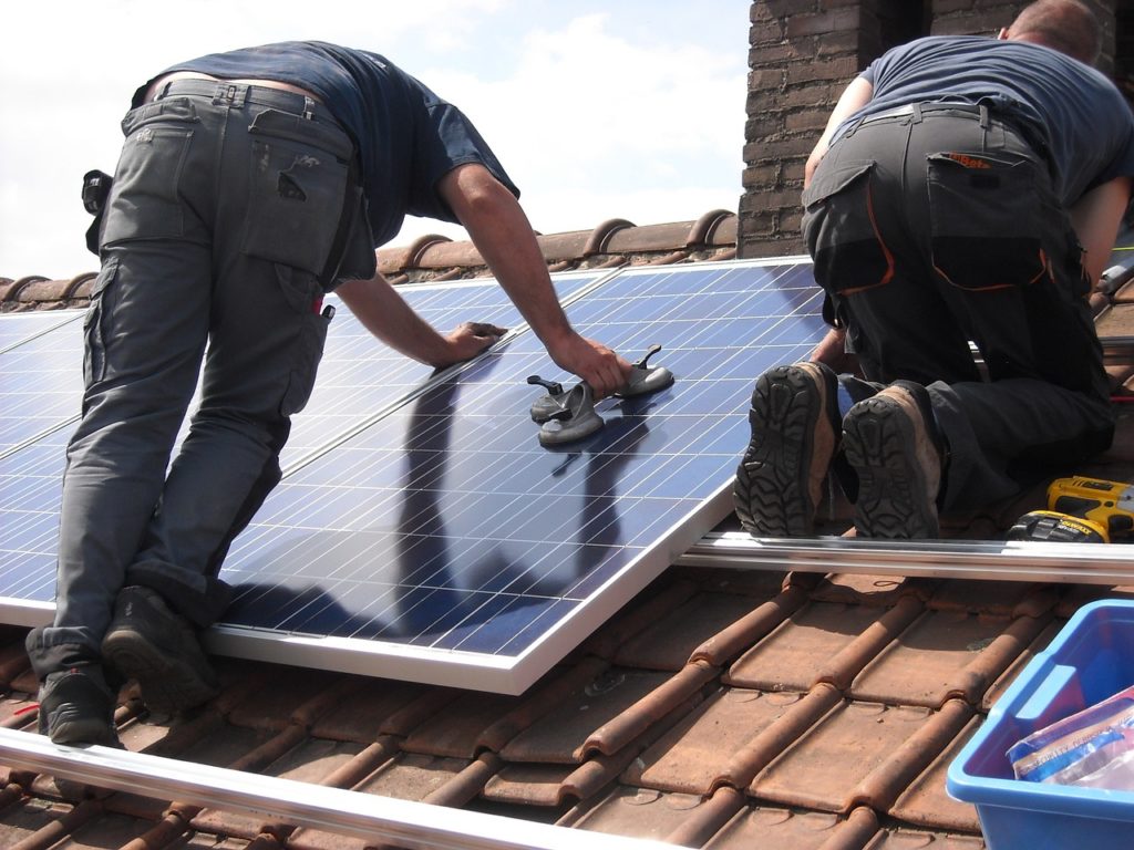 Two workers on a tiled roof of a home fitting new solar panels