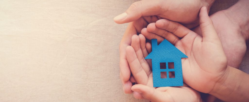 Adult and child's hands cupping a blue paper cut-out of a house.