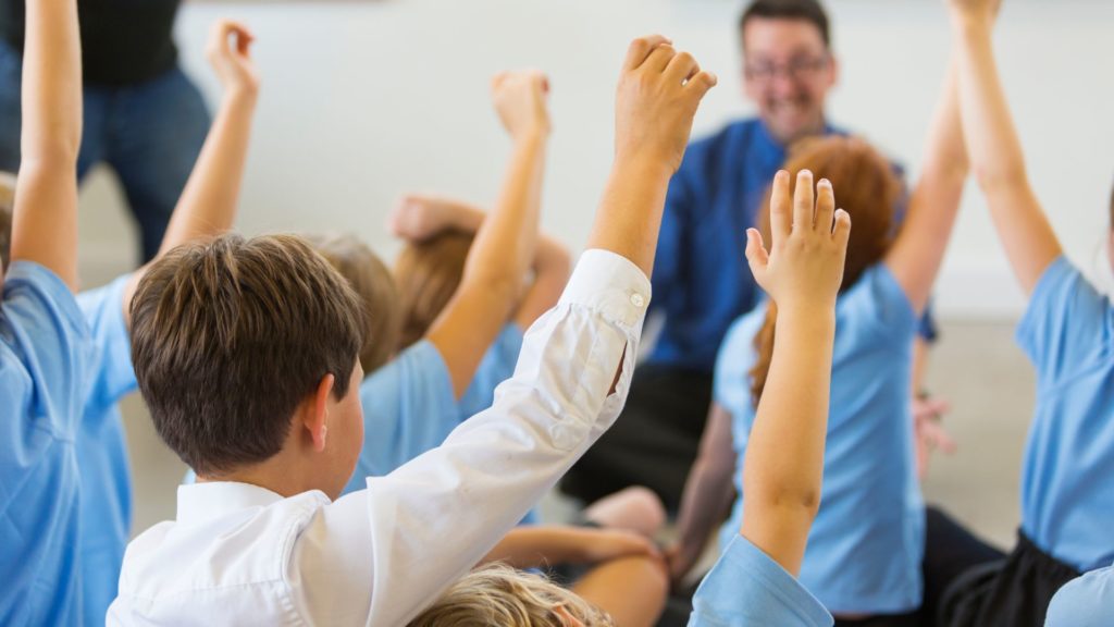 A group of children holding their hands up in a classroom.