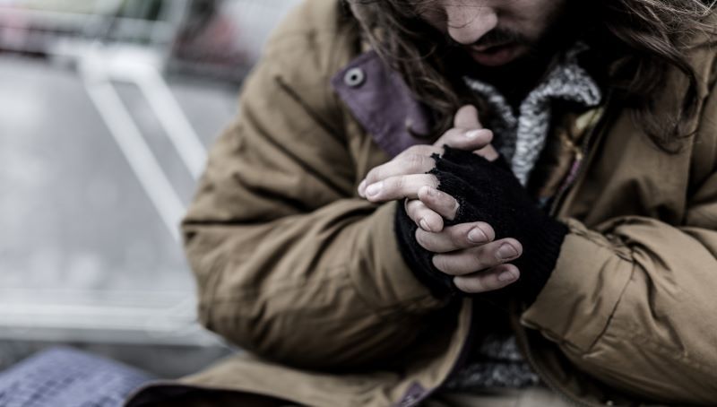 A homeless person wearing mittens rubbing their hands together in the cold.