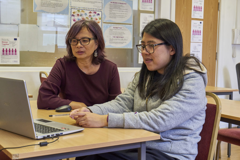 Two women interact on a laptop together.