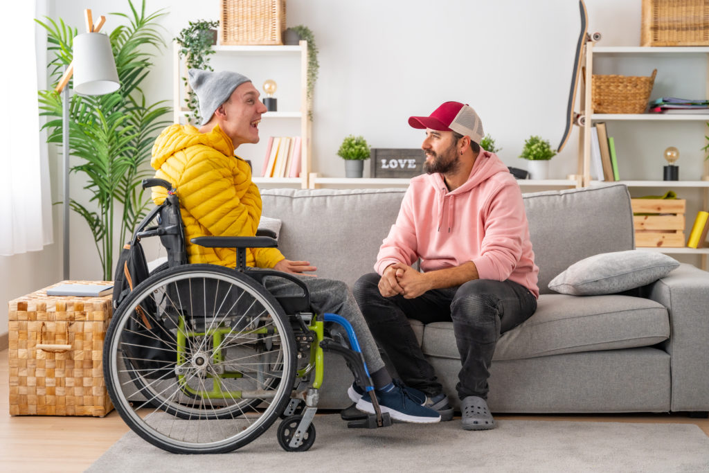 Disabled man in wheelchair and friends chatting relaxed in the living room of the house.